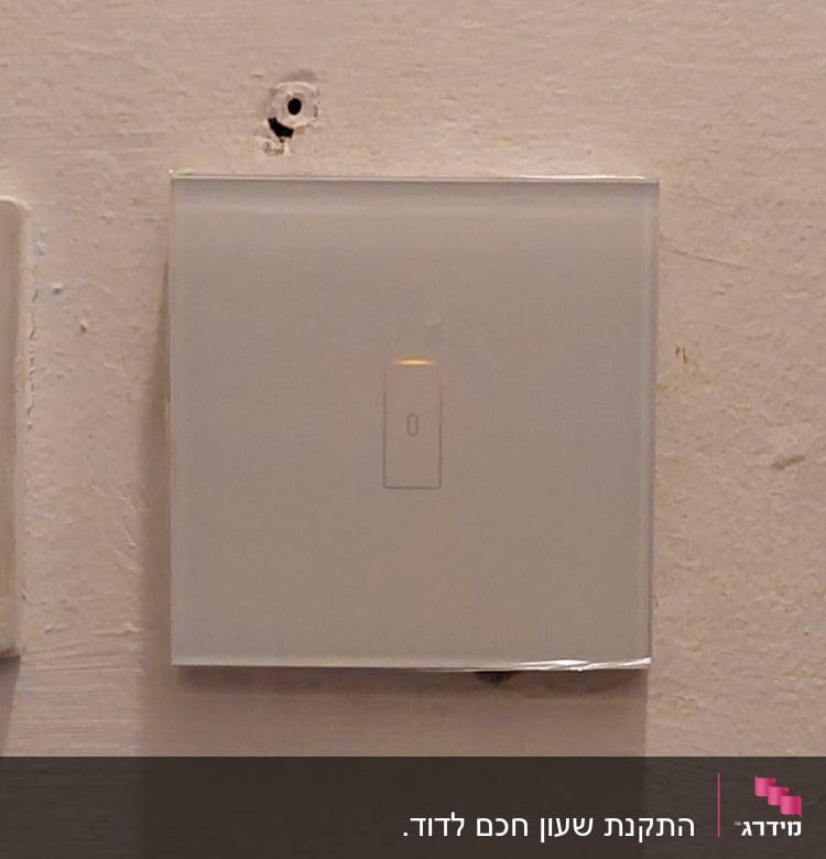 מתג חשמלי על קיר לבן עם חור מעליו